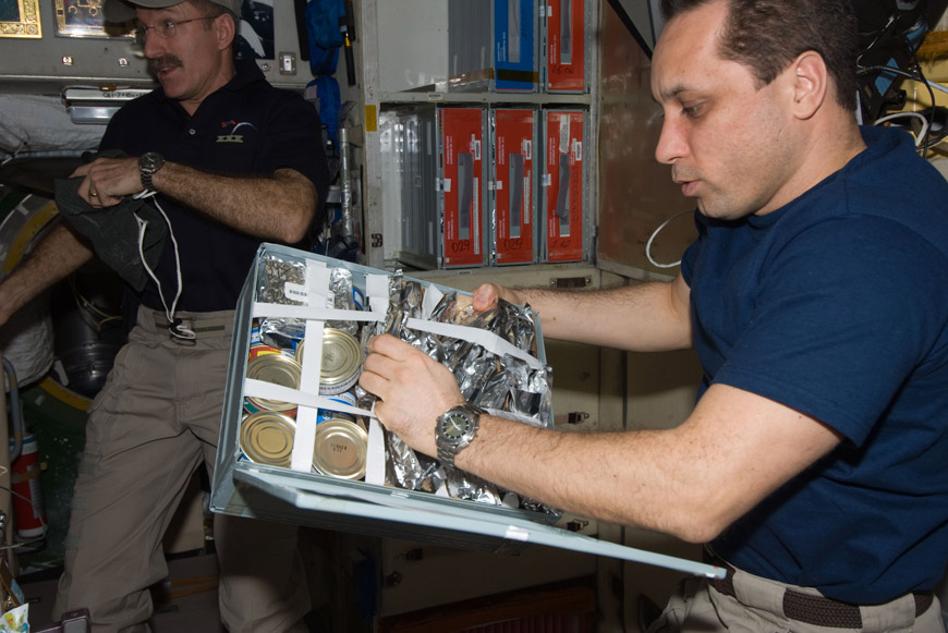 Космонавт Антон Шкаплеров достает из контейнера продукты. На заднем плане виден астронавт Дэн Бёрбэнк (Dan Burbank). 30-я экспедиция МКС, 2012 г. (фото NASA)
